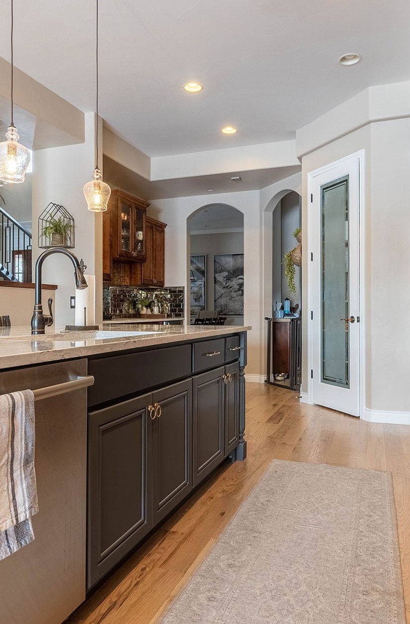 Kitchen with dark island cabinetry, marble worktop and wooden flooring leading to hallway