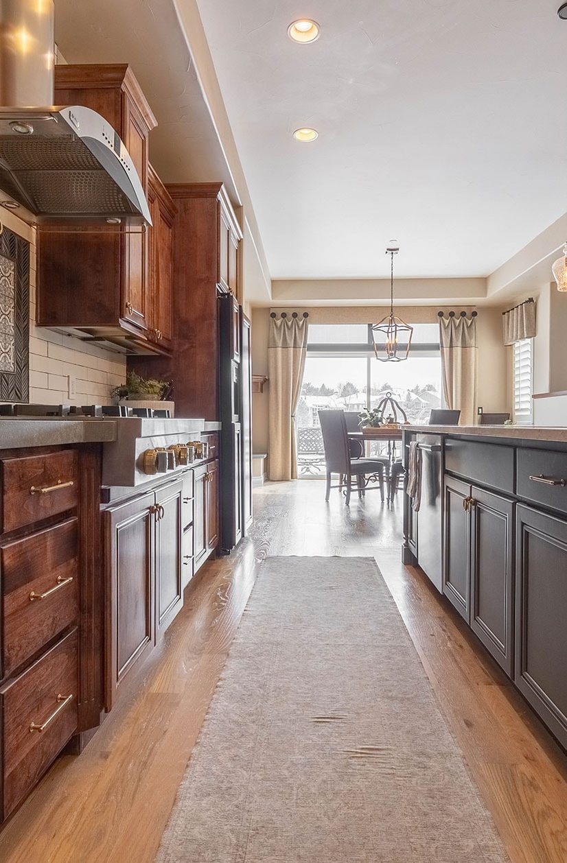 Long galley kitchen with wood cabinetry, central runner rug and dining space by large window