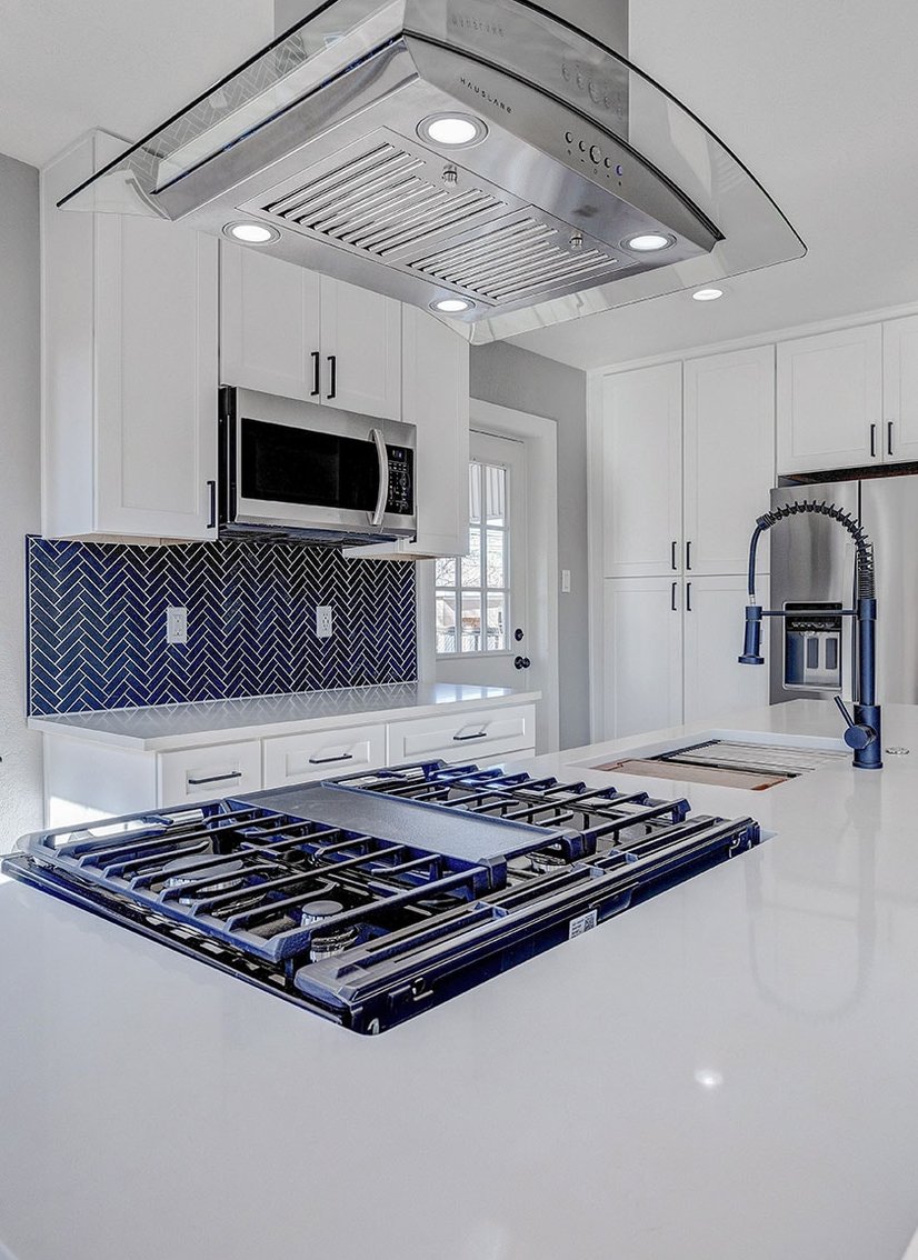 Modern white kitchen with glass canopy range hood, blue tile backsplash and gas hob on island